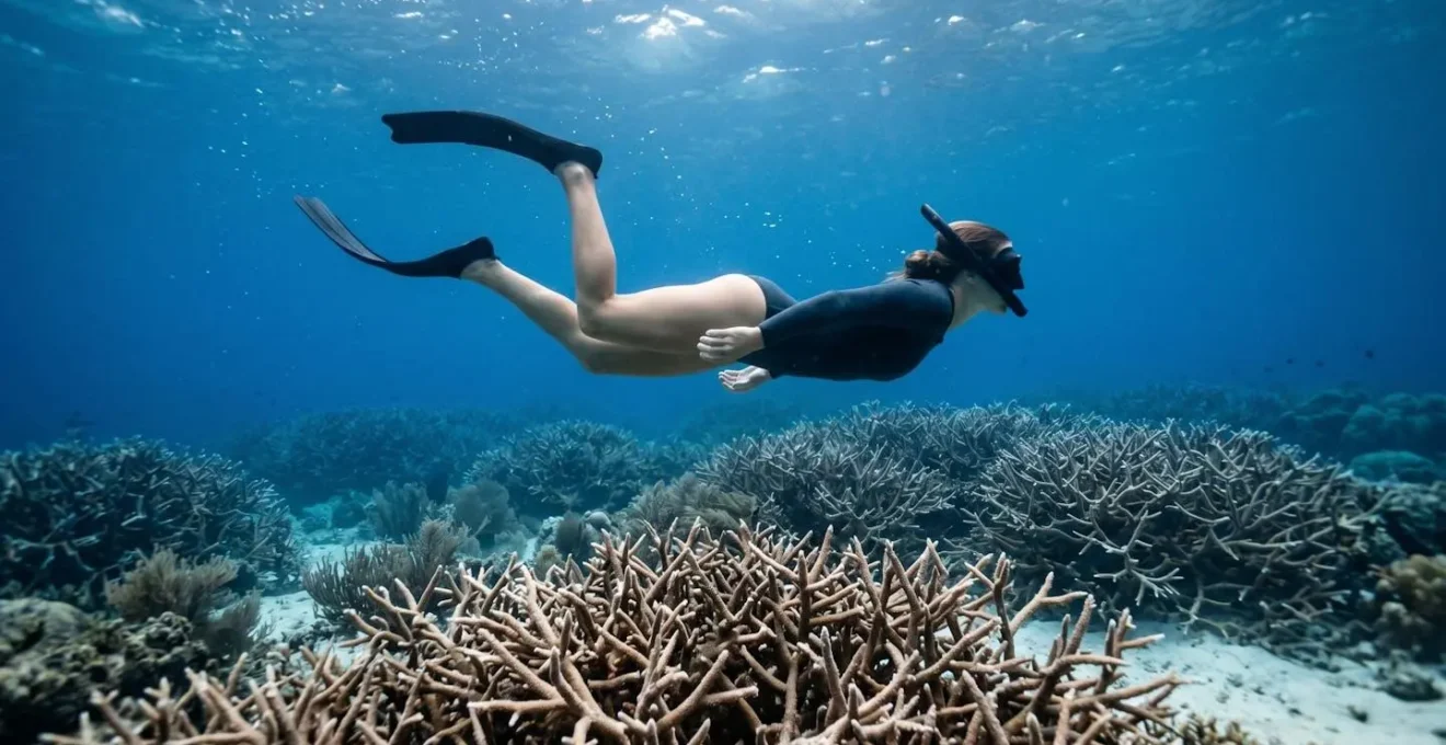 Underwater view of snorkeler demonstrating horizontal frog kick technique above delicate coral formations